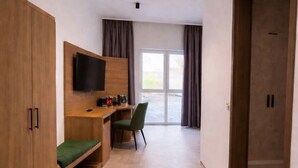 Une chambre d’hôtel moderne dotée d’une armoire en bois, d’un téléviseur à écran plat, d’un bureau avec une chaise et d’une grande porte coulissante donnant sur un balcon.