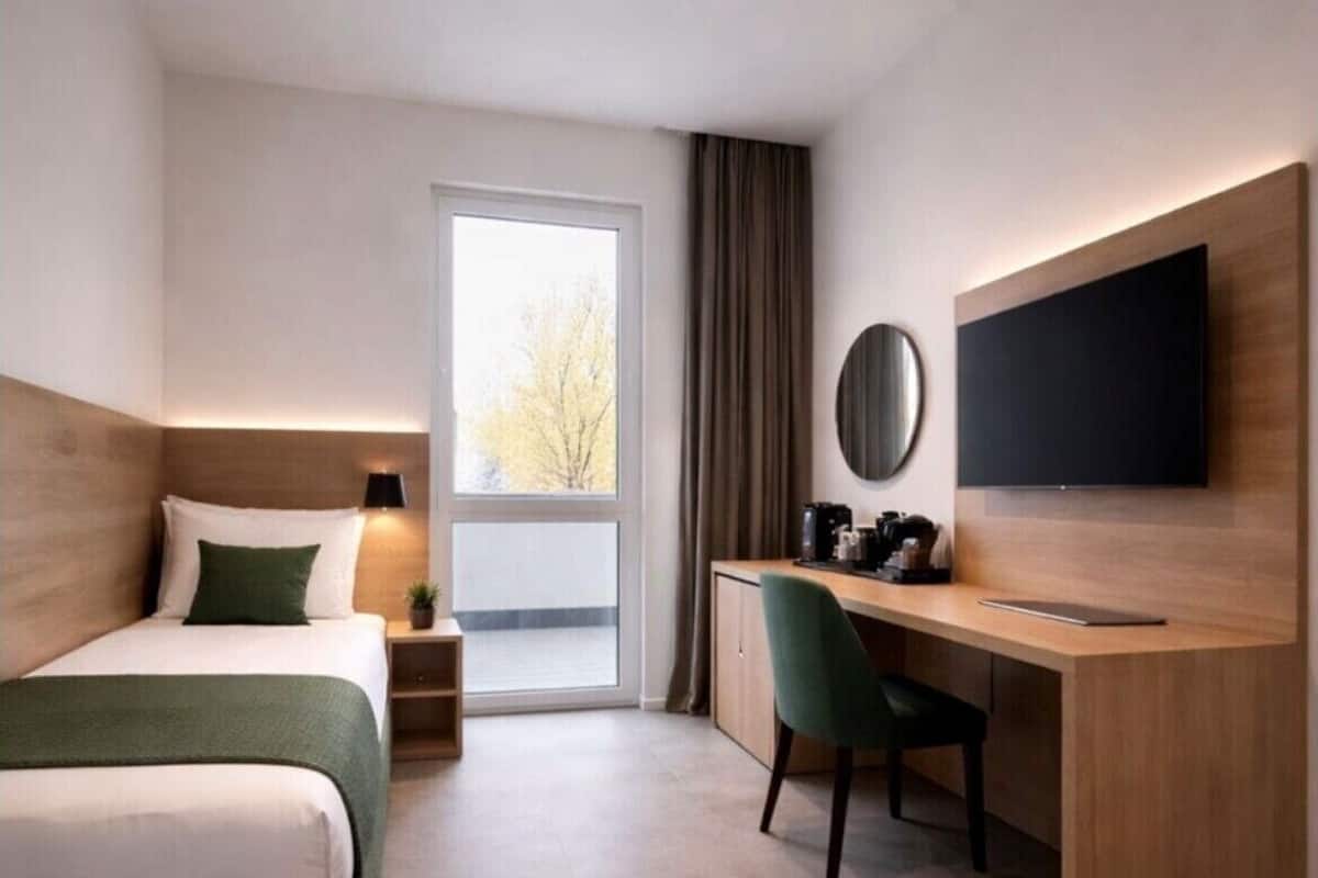 A hotel room with a bed, a desk, a chair, a TV, and a window.