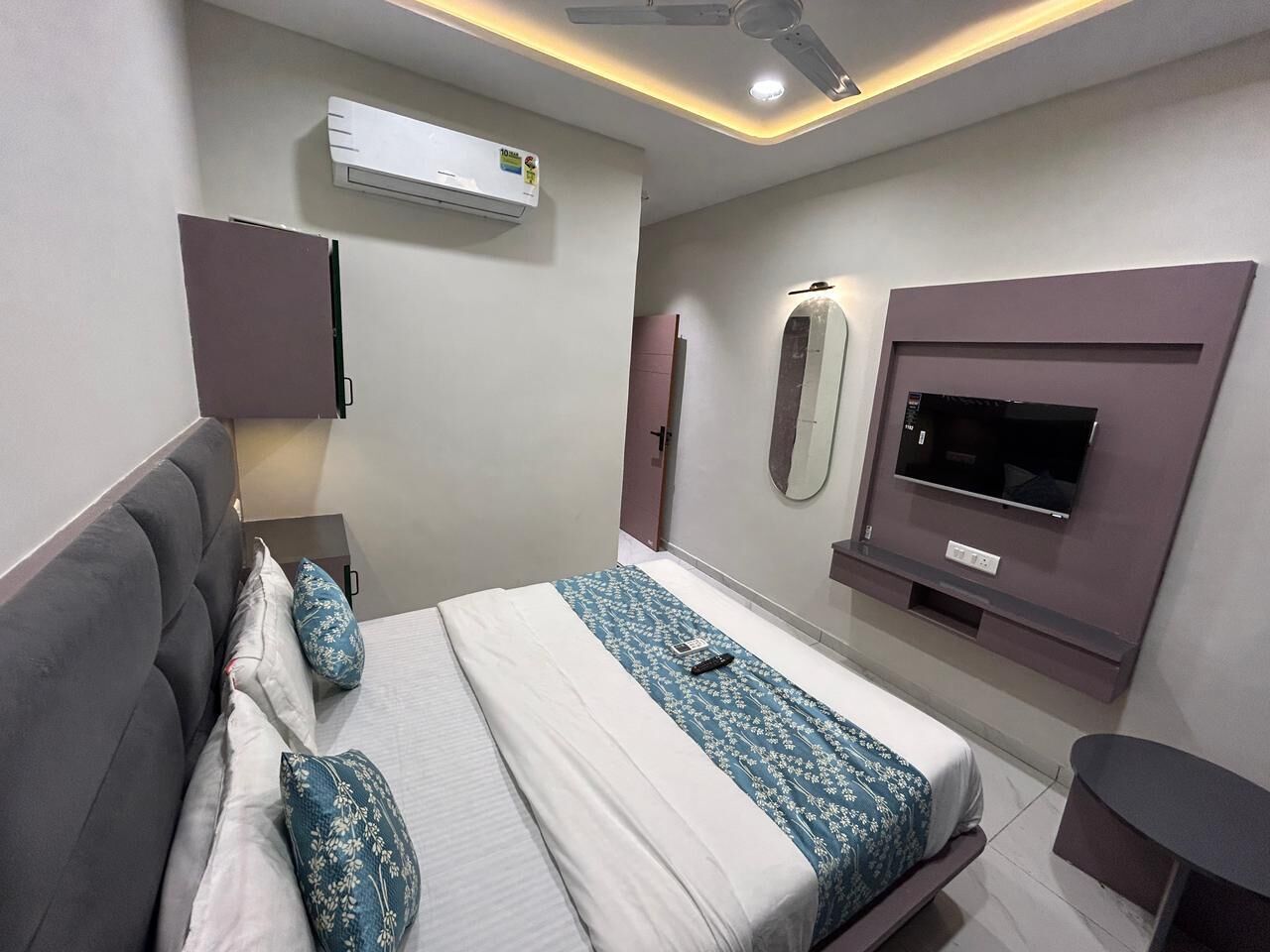 A modern hotel room with a bed, a TV, an air conditioning unit, and a ceiling fan.