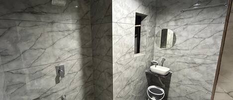 A bathroom with marble walls, a shower, a toilet, and a sink.
