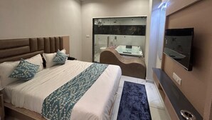 A modern hotel room with a large bed, a TV, a bathroom with a glass shower, and a ceiling fan. - Hotel Prime Elite (Ahmedabad)
