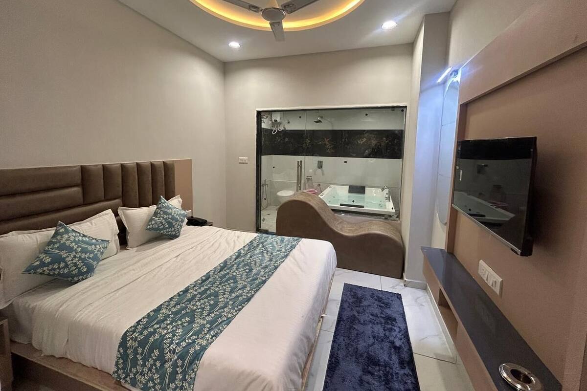 A modern hotel room with a large bed, a TV, a bathroom with a glass shower, and a ceiling fan.