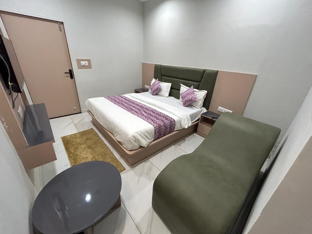 A compact hotel room with a bed, bedside table, and a small round table.