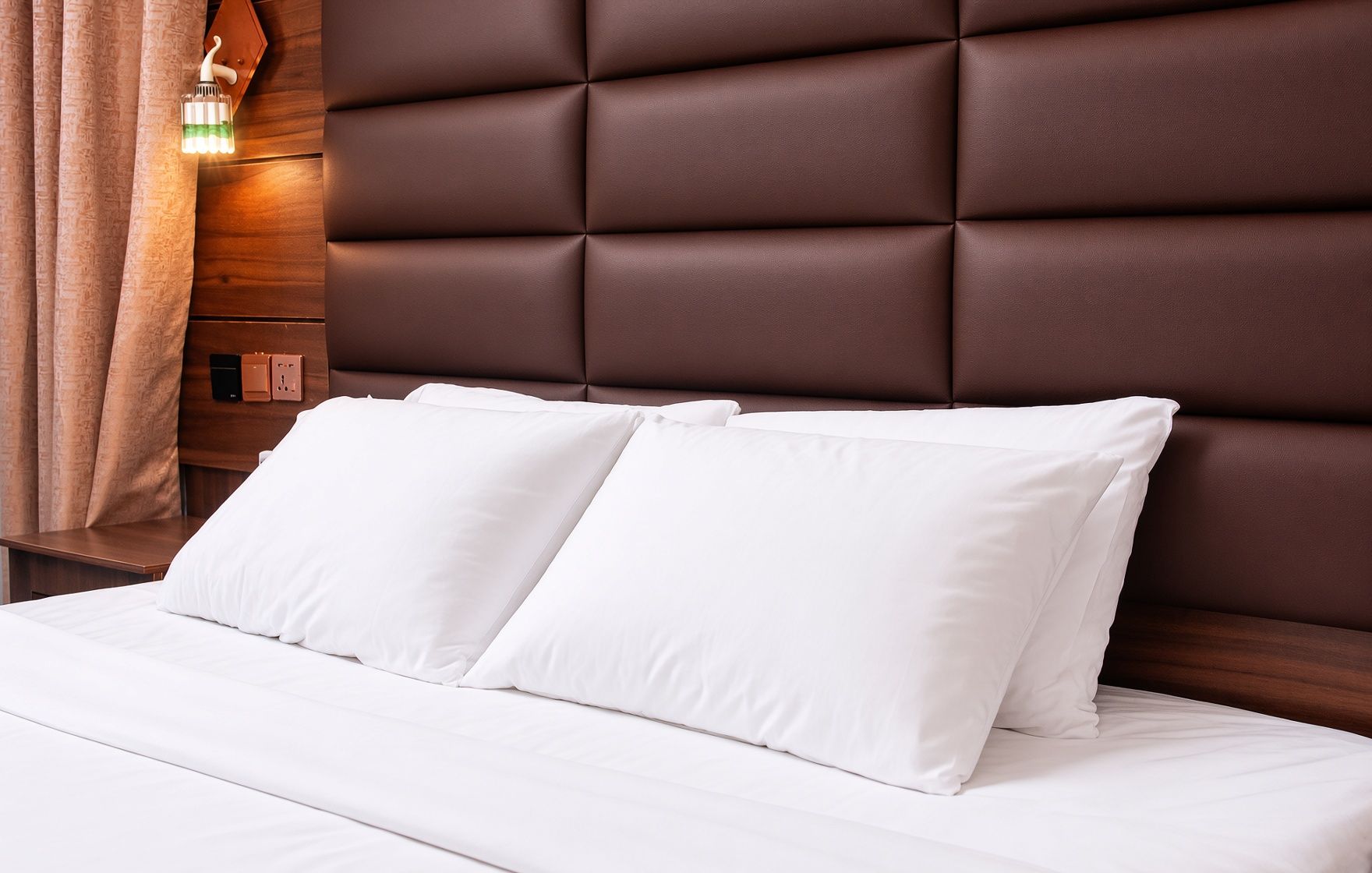 Una cama con ropa de cama blanca y un cabecero tapizado en marrón.