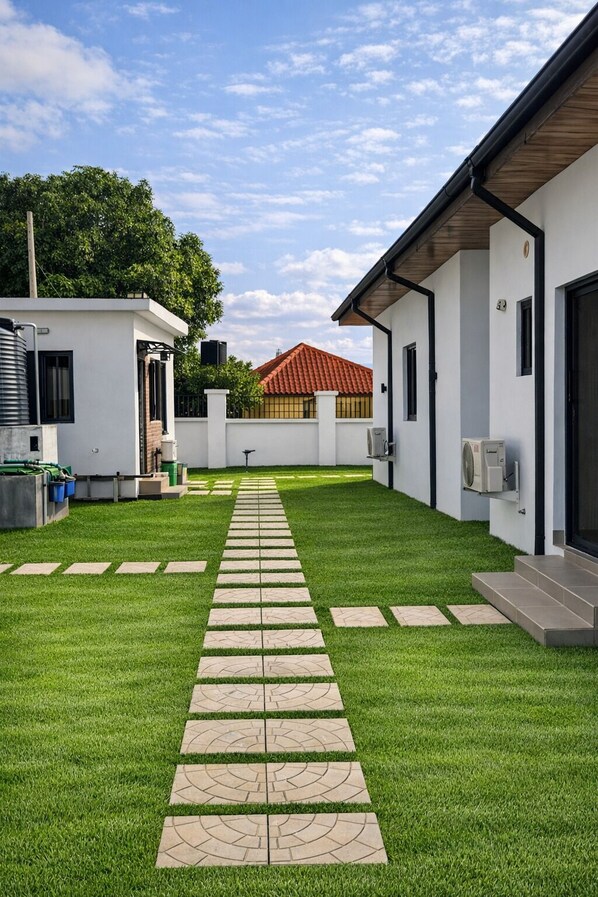 A modern building with a paved pathway leading to a door, surrounded by well-maintained grass and a clear sky.