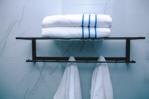 Un baño con pared de mármol, un perchero con toallas dobladas y otro perchero con dos toallas colgadas.