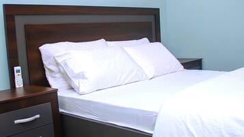 Ein ordentlich gemachtes Bett mit weißer Bettwäsche, einem Holzkopfende und einem Nachttisch mit Schubladen.