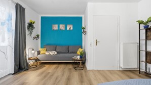 Un salon moderne avec un canapé gris, un mur d’accent bleu et une porte blanche.