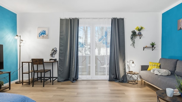 Un salon moderne comprenant un canapé, une table à manger avec des chaises, une table basse et une grande fenêtre avec des rideaux.