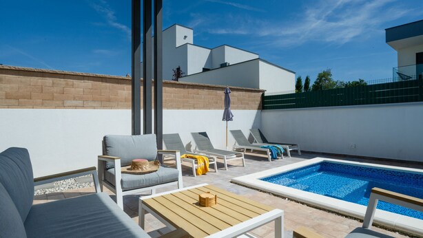 A rooftop pool area with lounge chairs, a small table, and a view of a modern building. - Villa Tony by Villas Guide (Peroj)