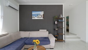 A modern living room with a white sofa, a blue accent, a bookshelf, and a painting of a coastal scene. - Villa Tony by Villas Guide (Peroj)