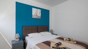 A bedroom with a bed, nightstands, a lamp, a painting, and a folded towel. - Villa Tony by Villas Guide (Peroj)