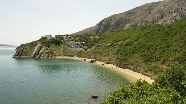 Eine Küstenlandschaft mit Strand, Häusern auf einer Klippe und freiem Blick auf das Meer.