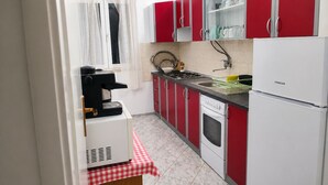 Eine kleine Küche mit roten Schränken, einem weißen Kühlschrank, einer Kaffeemaschine und einem Fliesenboden.