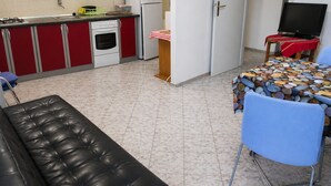 Eine kleine Küche mit Herd, Backofen und Kühlschrank, ein Essbereich mit Tisch und Stühlen sowie eine Wohnbereich mit einer Couch.