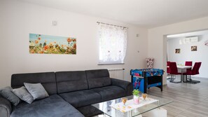 A modern living room with a sofa, a glass coffee table, a foosball table, and a dining area with red chairs. - Villa Butkovici by Villas Guide (Marcana)