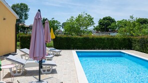 A swimming pool with lounge chairs and umbrellas, surrounded by greenery and a building. - Villa Butkovici by Villas Guide (Marcana)