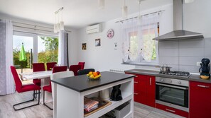 A modern kitchen with red cabinets, a gas stove, and a dining area with red chairs. - Villa Butkovici by Villas Guide (Marcana)