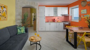 A modern kitchen with white cabinets, a dining area with a wooden table and yellow chairs, a gray sofa with a green pillow, and a stone wall. - Apartment Lemon&Soul by Villas Guide (Crikvenica)