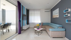 Una sala moderna con un sofá, un televisor y una zona de comedor con sillas.