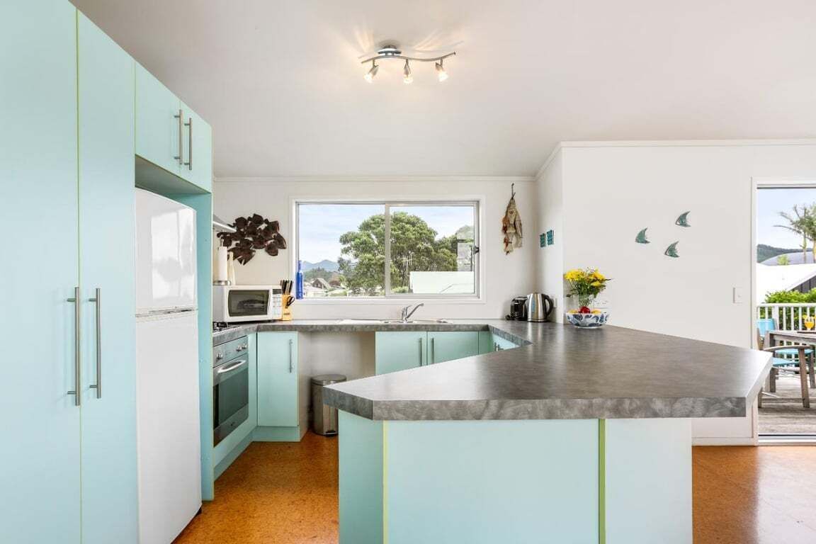 Une cuisine avec des meubles de couleur bleu clair, un îlot central, une fenêtre donnant sur un beau paysage et une plante suspendue.