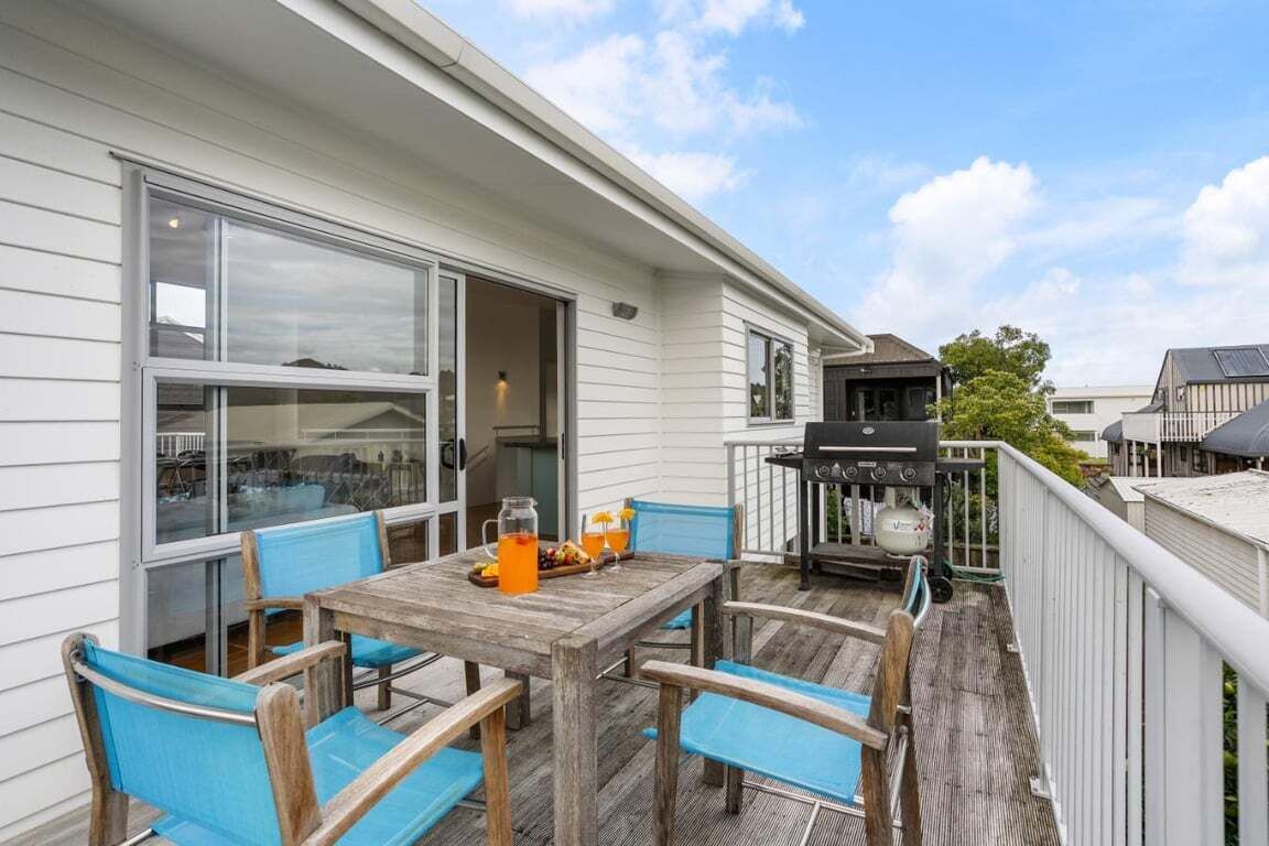 A wooden deck with a table and chairs, a grill, and a large window.