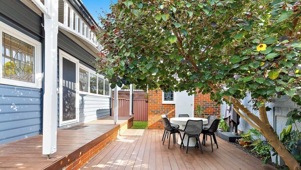 A backyard with a wooden deck, a round table with chairs, and a tree providing shade.