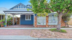 A residential house with a covered porch, a brick facade, and a white picket fence.