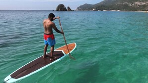 Una persona haciendo paddleboard sobre aguas turquesas cristalinas, con montañas al fondo.
