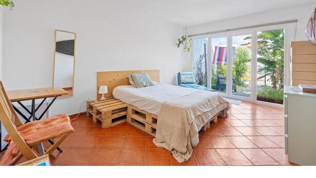 Un dormitorio con una cama, una silla de madera, un escritorio y un ventanal grande.