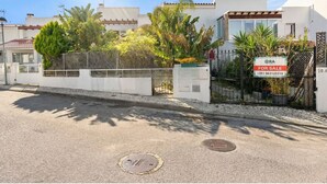 Una propiedad residencial con entrada protegida por un portón, una tapa de registro en la acera y un cartel de 'For Sale'.