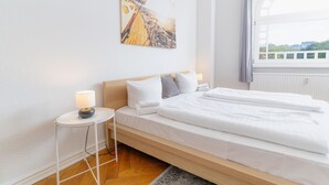 A hotel room with a bed, a nightstand, a lamp, a painting, and a window. - fewo1846 - Strandkoje / luxurious old apartment for max 5 persons with sea view (Flensburg)