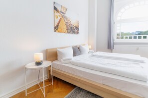 A hotel room with a bed, a nightstand, a lamp, a painting, and a window. - fewo1846 - Strandkoje / luxurious old apartment for max 5 persons with sea view (Flensburg)