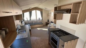 Cocina compacta para vehículos recreativos, con estufa, horno y zona de comedor con mesa y sillas.