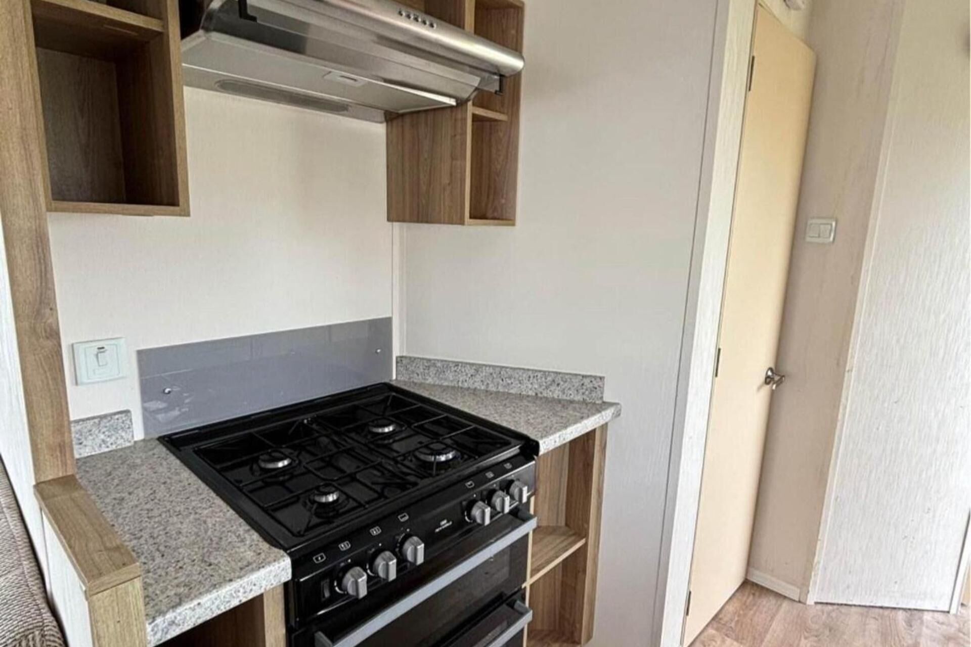 A compact kitchen with a gas stove, oven, and a stainless steel range hood.