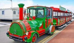 Ein farbenfroher Zug mit grüner und roter Außenfarbe, einem sichtbaren Schlot und einem Personenwagen mit rotem Dach.