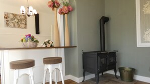 Uma cozinha com fogão preto, dois bancos de bar brancos, bancada de madeira e um vaso com flores.
