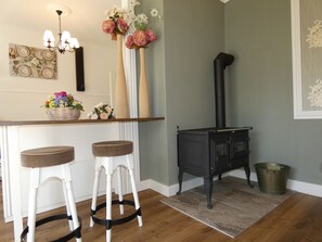 A kitchen with a black stove, two white bar stools, a wooden countertop, and a vase with flowers. - fewo1846 - Romance - Gelting (Gelting)