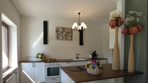 Uma cozinha com armários brancos, bancada de madeira, forno embutido, pia, lustre e vasos decorativos com flores.