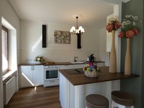 A kitchen with white cabinetry, a wooden countertop, a built-in oven, a sink, a chandelier, and decorative vases with flowers. - fewo1846 - Romance - Gelting (Gelting)