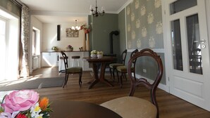 Uma sala de jantar com mesa e cadeiras de madeira, um candelabro e vista para a cozinha.