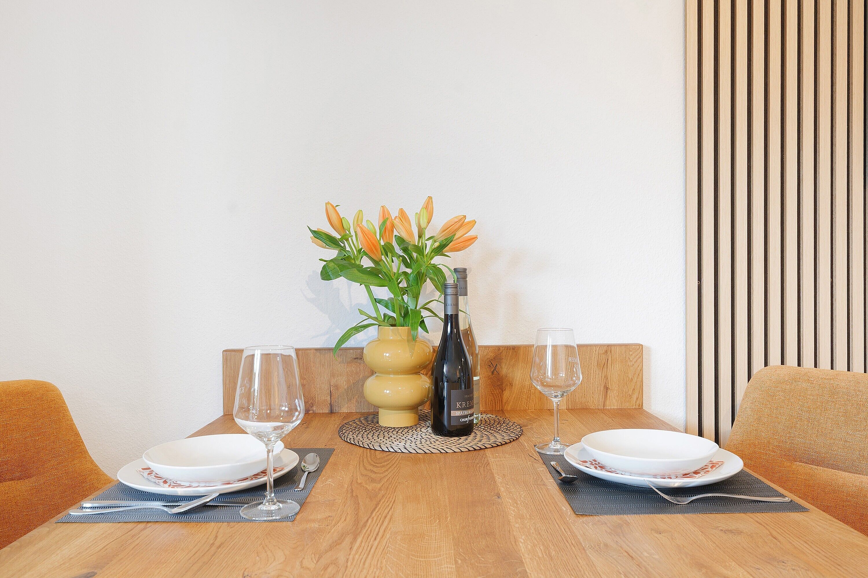 Una mesa de comedor con platos, una botella de vino y un florero con flores.