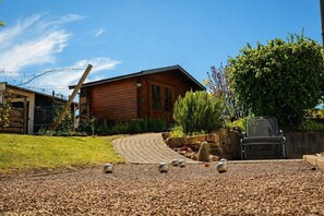 Una cabaña de madera con camino de grava, una silla de metal y un muro de piedra.