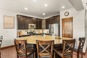 A kitchen with dark wood cabinets, a granite island, stainless steel appliances, and a wooden door. - NEW! Ski-In/Out Granby Ranch・Sleeps 16 ・Arcade (Granby)