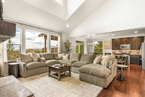 A spacious living room with a sectional sofa, a coffee table, and a view of the outdoors through large windows. - NEW! Ski-In/Out Granby Ranch・Sleeps 16 ・Arcade (Granby)