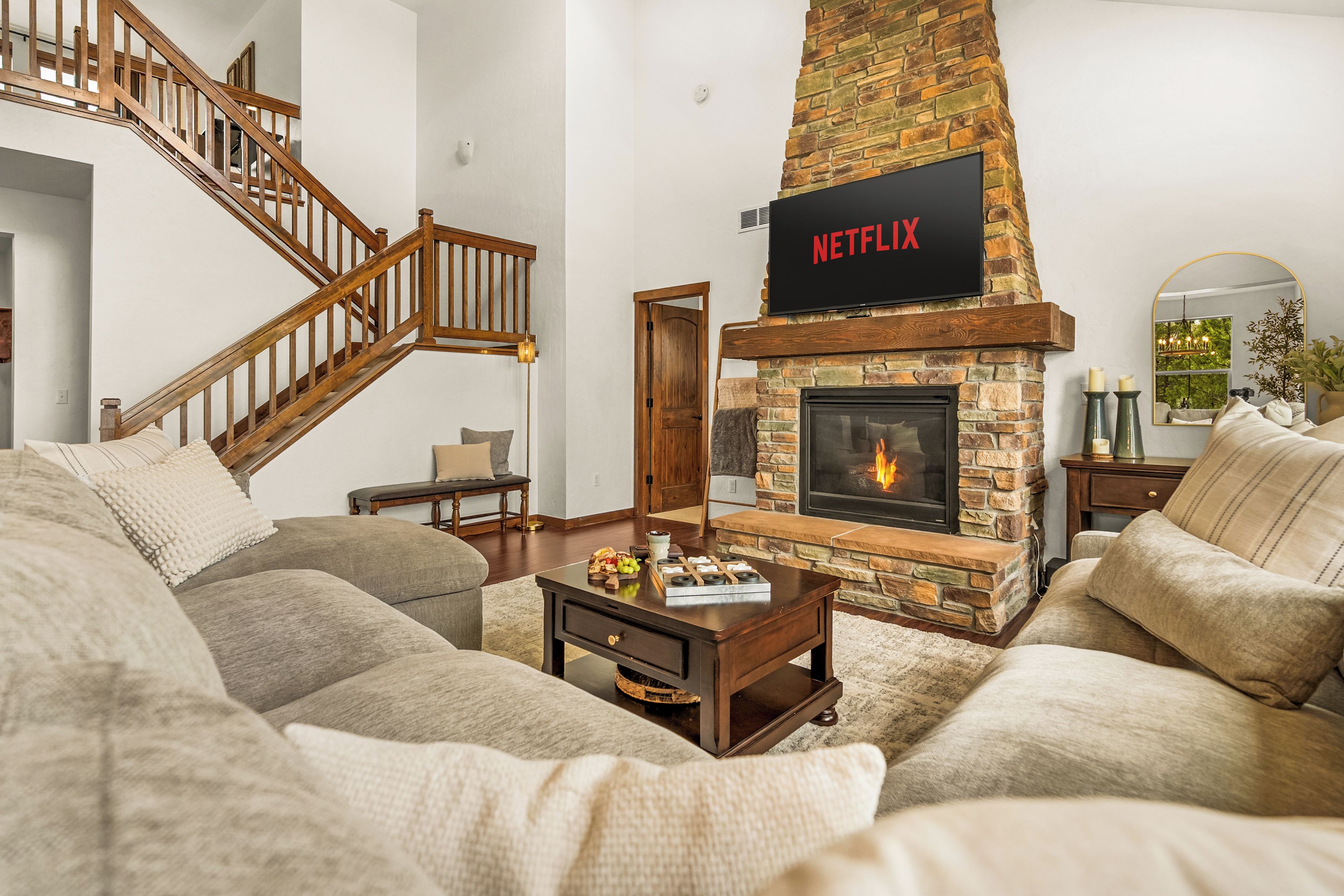 Un salon avec une cheminée en pierre, un logo Netflix, un escalier et un canapé confortable.