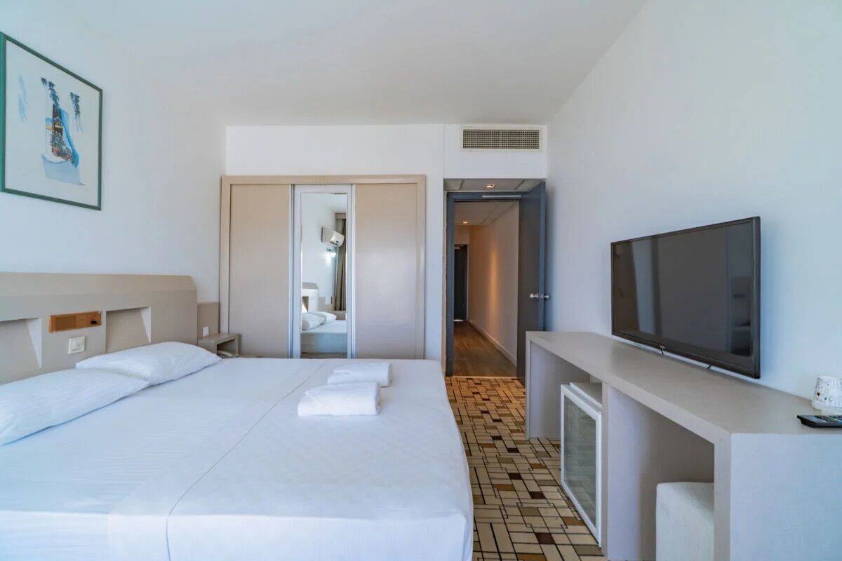 Una habitación de hotel con cama, televisión, baño con espejo y un pasillo.