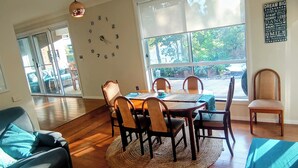 A dining area with a wooden table, chairs, a clock, and a view through large windows. - 3BR Bushland Retreat, Relax/ Professional Stay–near the bay & CBD/ Private Deck (North Batemans Bay)