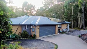 A single-story house with a garage, surrounded by trees and a gravel driveway. - 3BR Bushland Retreat, Relax/ Professional Stay–near the bay & CBD/ Private Deck (North Batemans Bay)