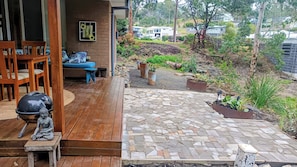 Una terraza de madera con un camino de piedra que conduce a un área de estar con un sofá azul y sillas de madera.